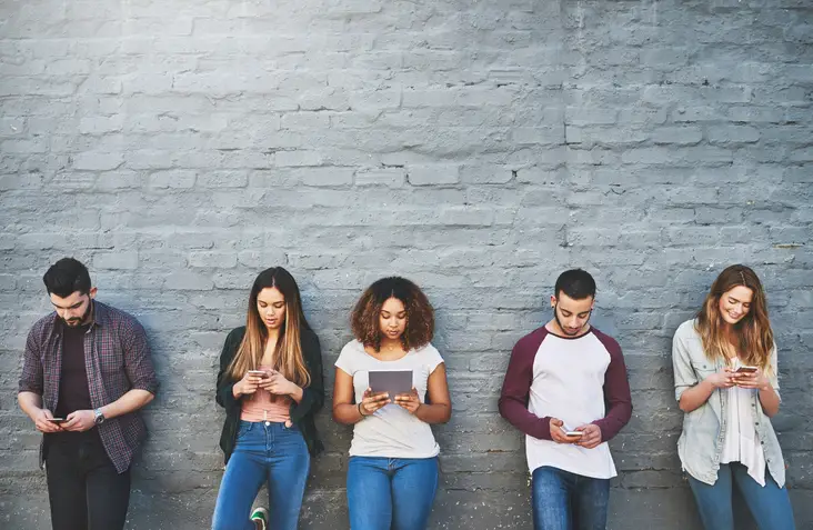 Five people using phones against wall